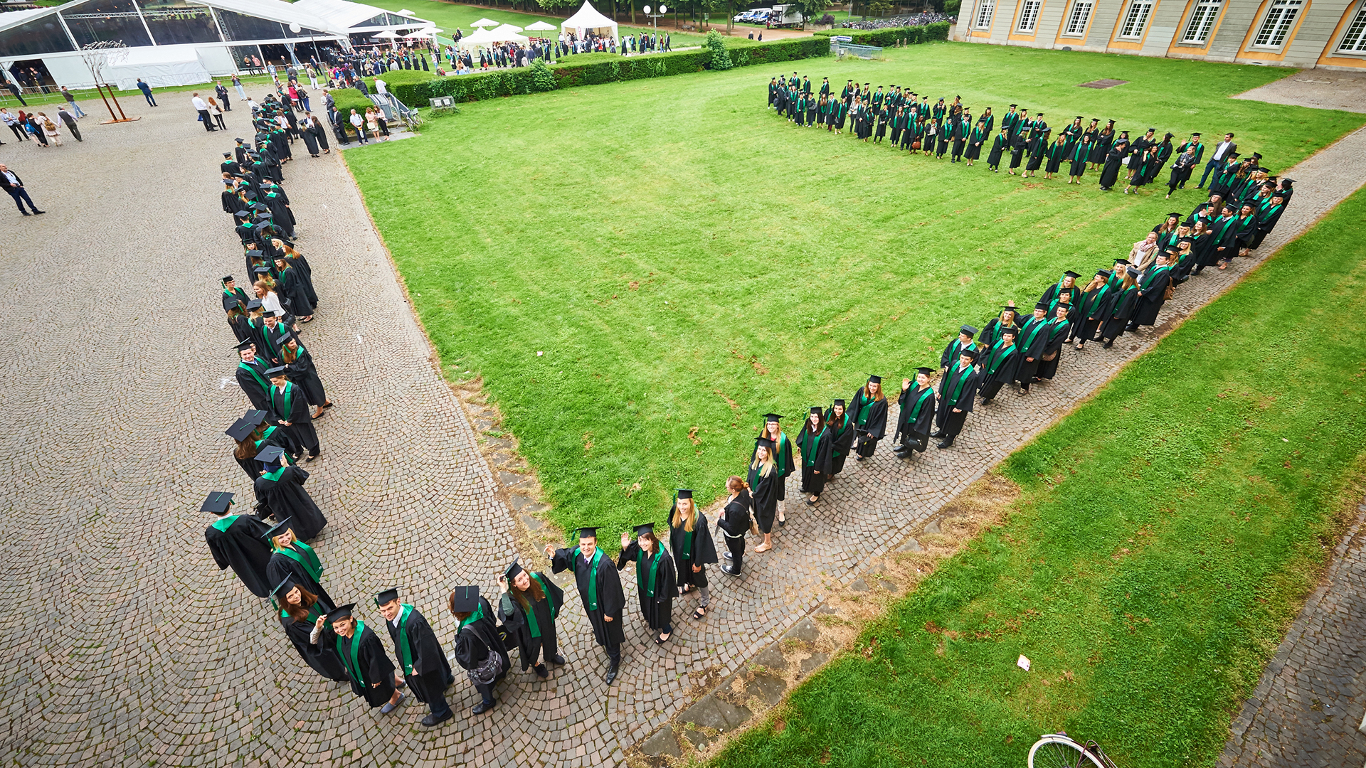 Eine Wissenschaftlerin und ein Wissenschaftler arbeiten hinter einer Glasfassade und mischen Chemikalien mit Großgeräten.
